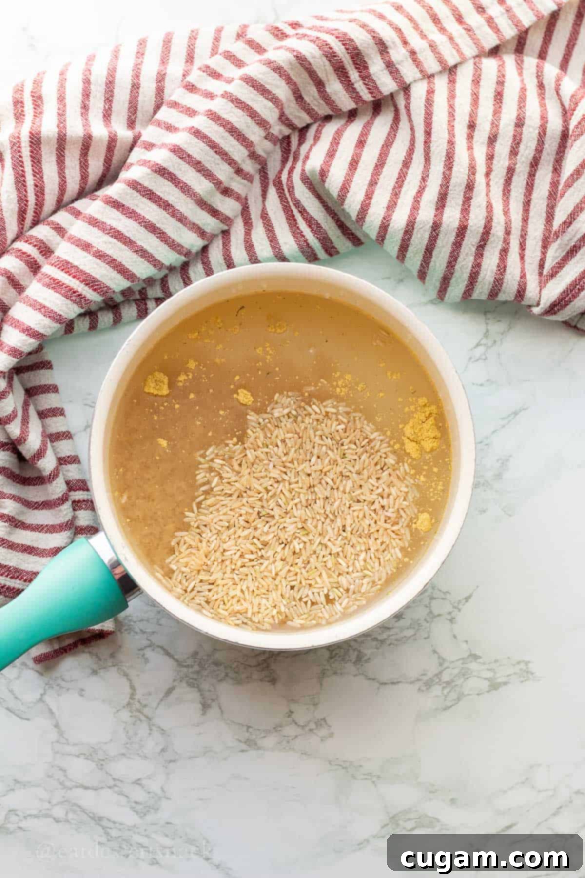 Uncooked brown rice with water and chicken bouillon in metal pan.