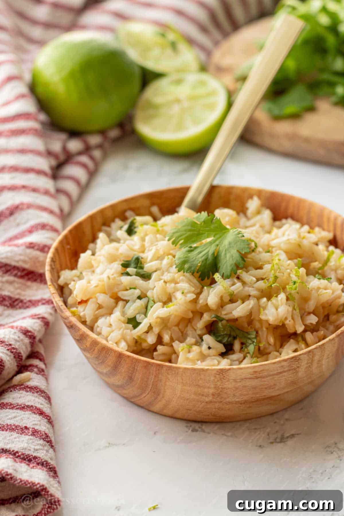Cooked brown rice with lime zest and cilantro in wood bowl with spoon.