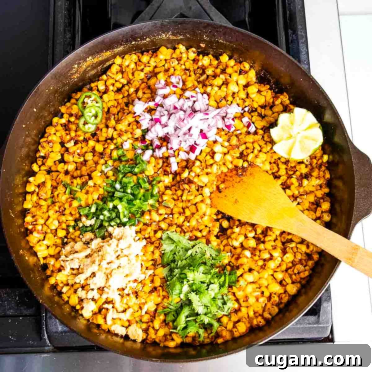 Delicious Vegan Mexican Street Corn 13 Cast iron skillet filled with corn, fresh herbs, onions, cooking on the stove, beginning to char.