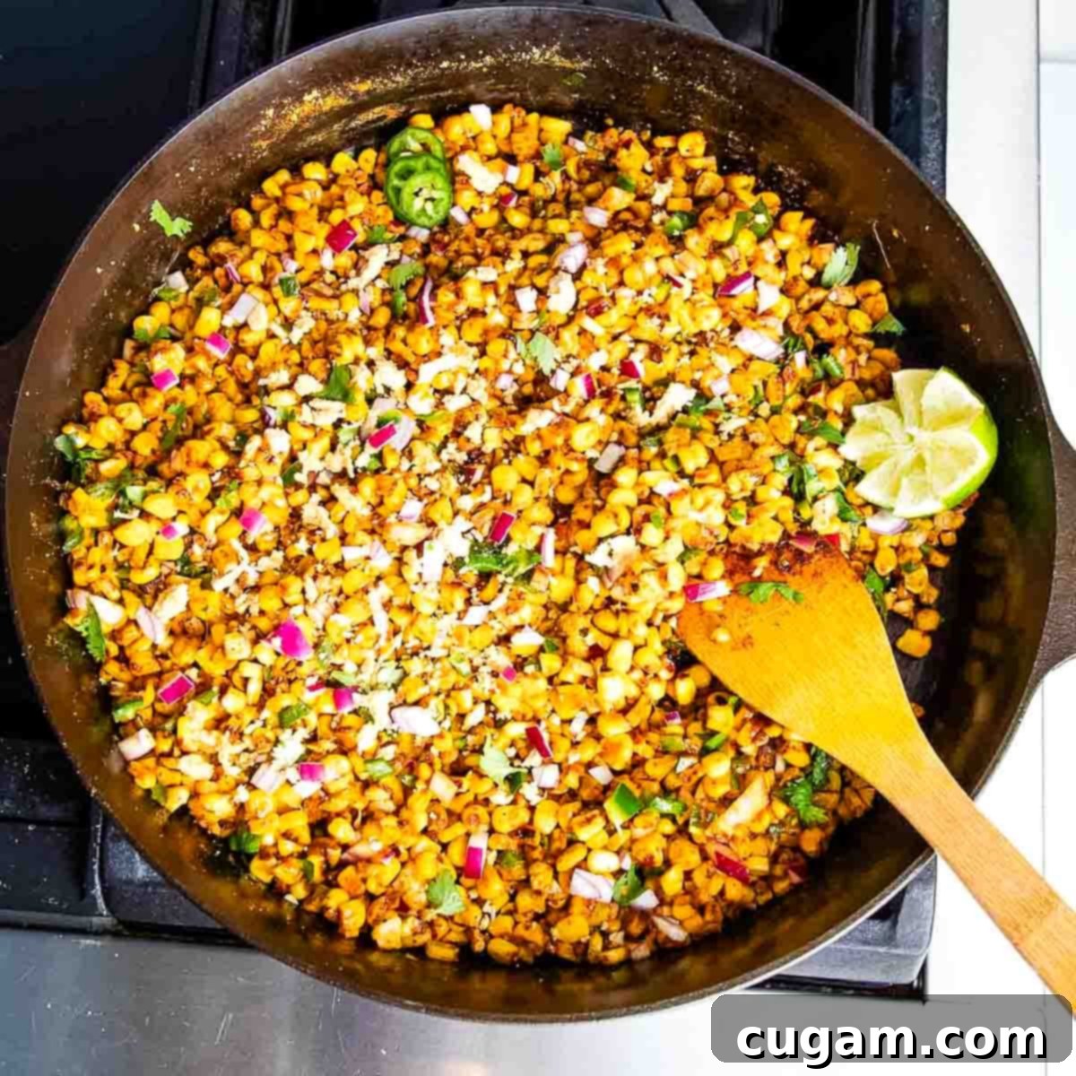Delicious Vegan Mexican Street Corn 14 Skillet filled with Mexican street corn, spices, and a wooden spatula, showing the charred kernels.