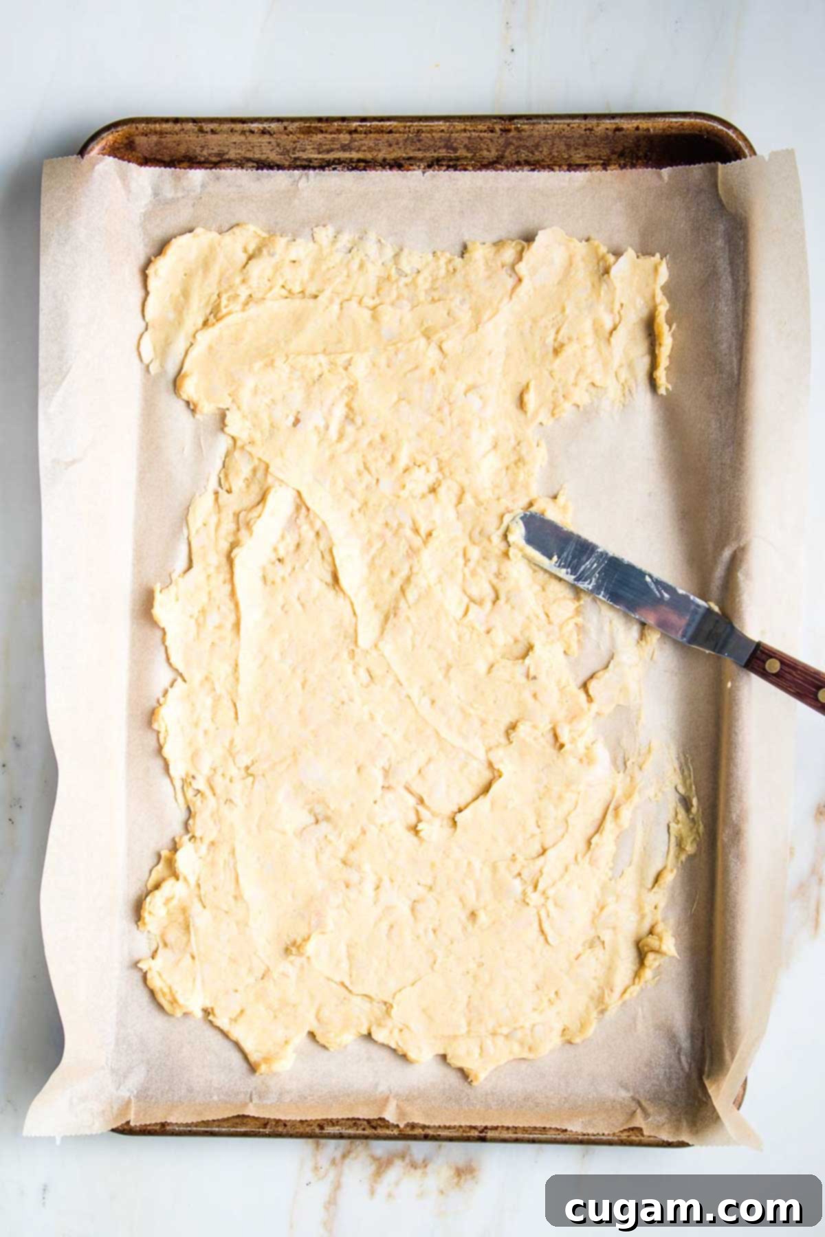 Delicious Vegan Mexican Street Corn 9 An offset spatula spreading the bean paste onto a parchment-lined baking sheet.
