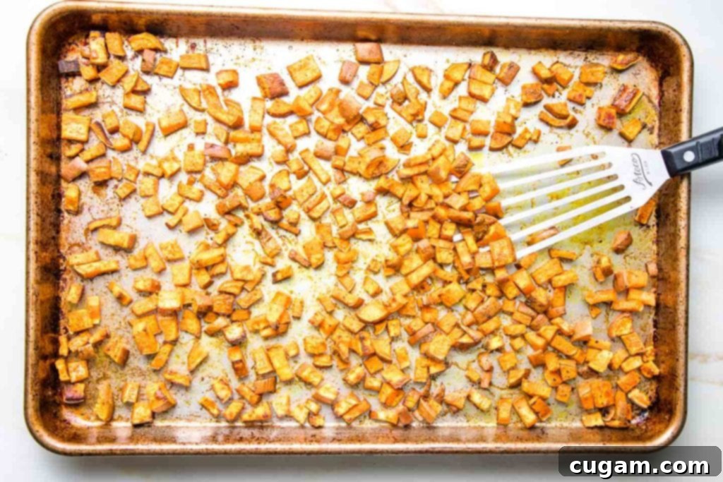 Large rimmed baking tray with small dice sweet potatoes that have been roasted with spices. 
