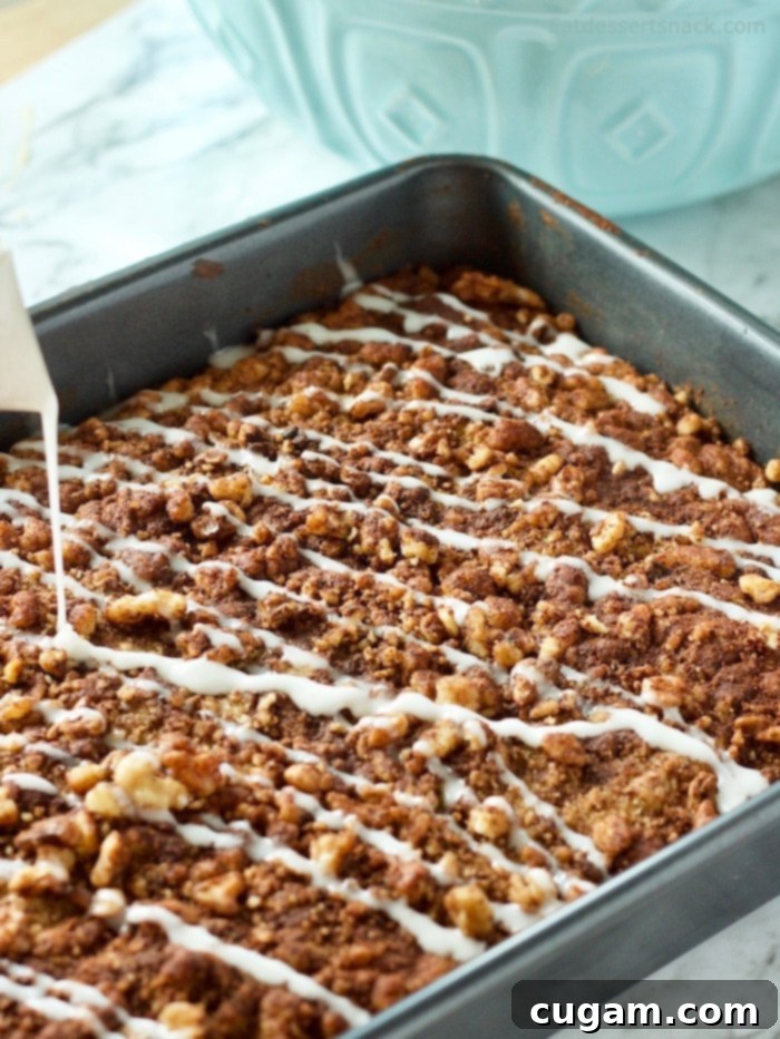 White glaze pouring over baked banana coffee cake in a dark pan. 