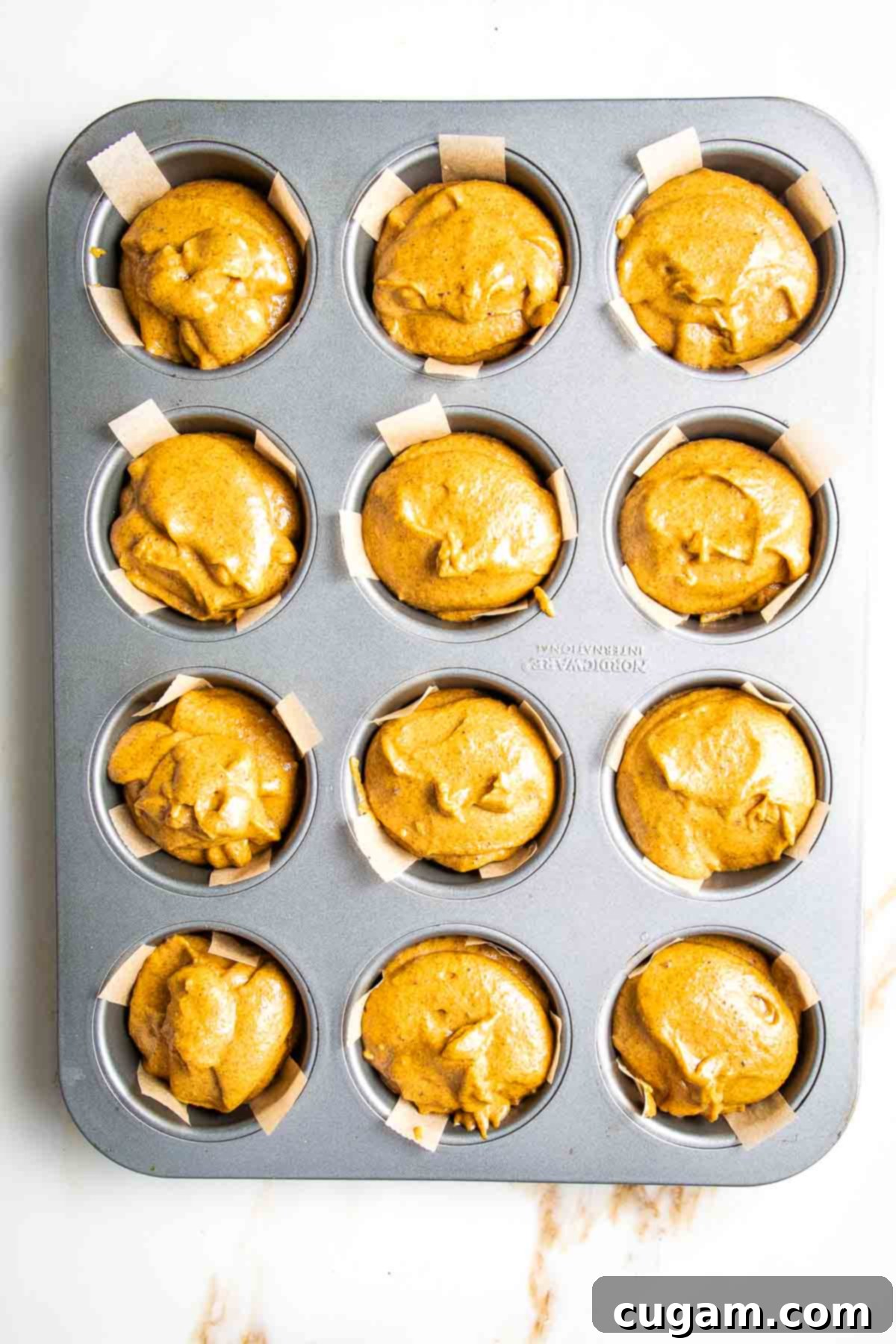 Pumpkin muffin batter, poured into muffin tins lined with parchment paper strips.