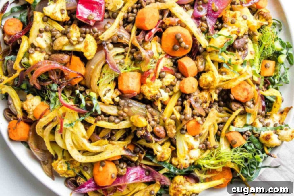 A large white bowl filled with brightly colored roasted red onions, carrots, fennel, and cauliflower, expertly mixed with dark lentils, vibrant green pistachios, and plump raisins.