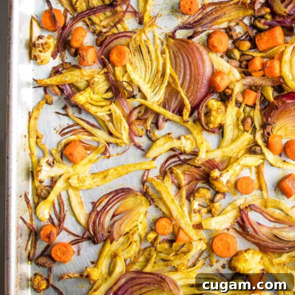 A sheet pan loaded with beautifully roasted, caramelized fennel wedges, red onion slices, carrot rounds, and cauliflower florets, mixed with pistachios, after being tossed in an aromatic spice marinade.