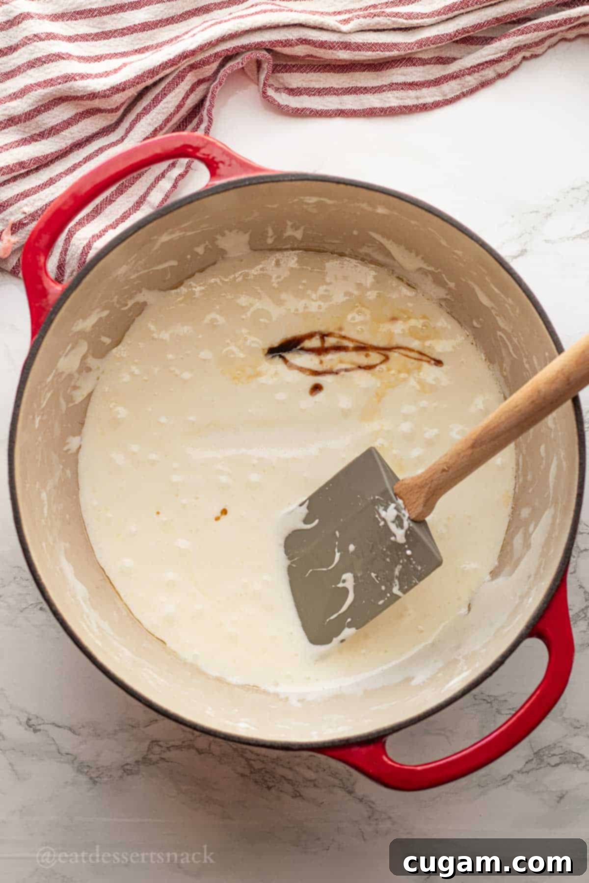 Melted marshmallows and butter in a red pot with vanilla extract and salt being added.