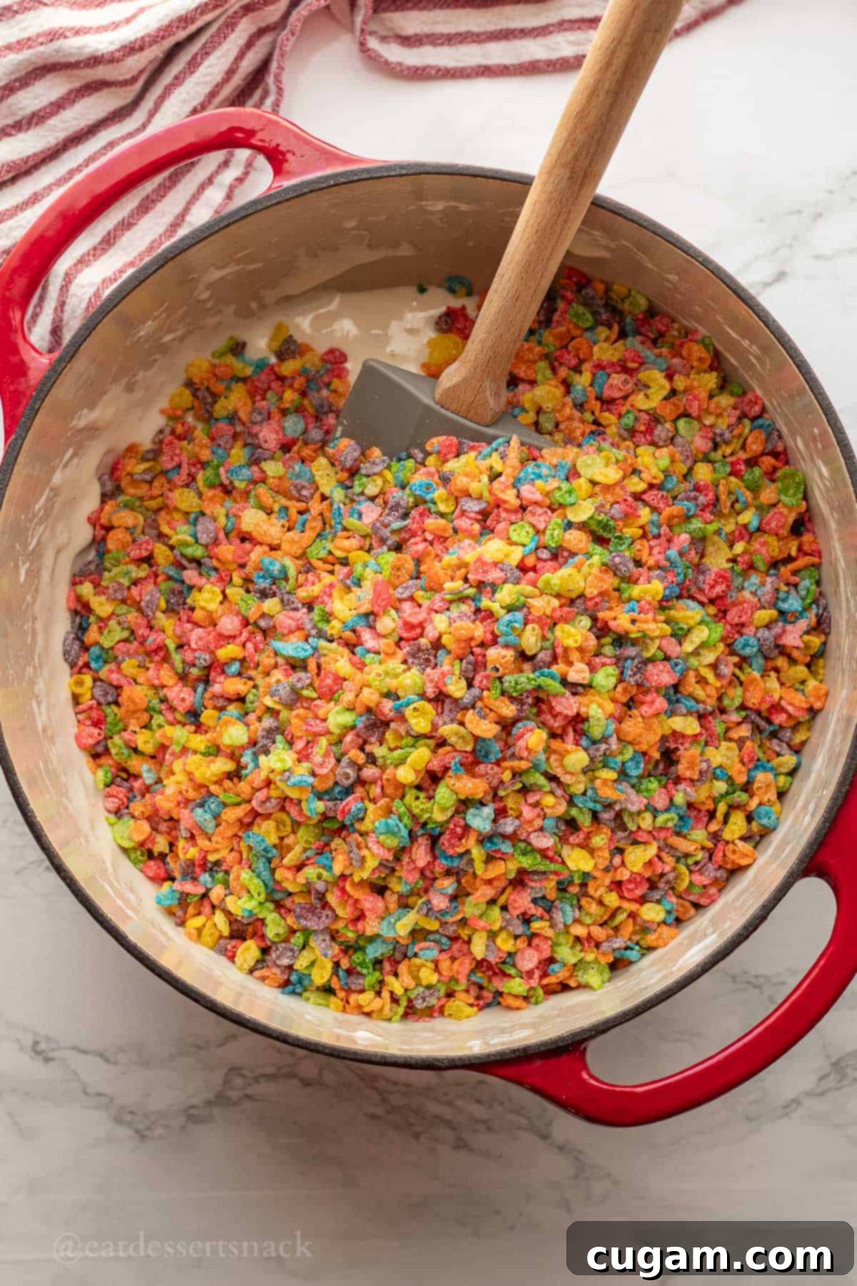 Fruity Pebbles cereal being added to the marshmallow mixture in a red pot.
