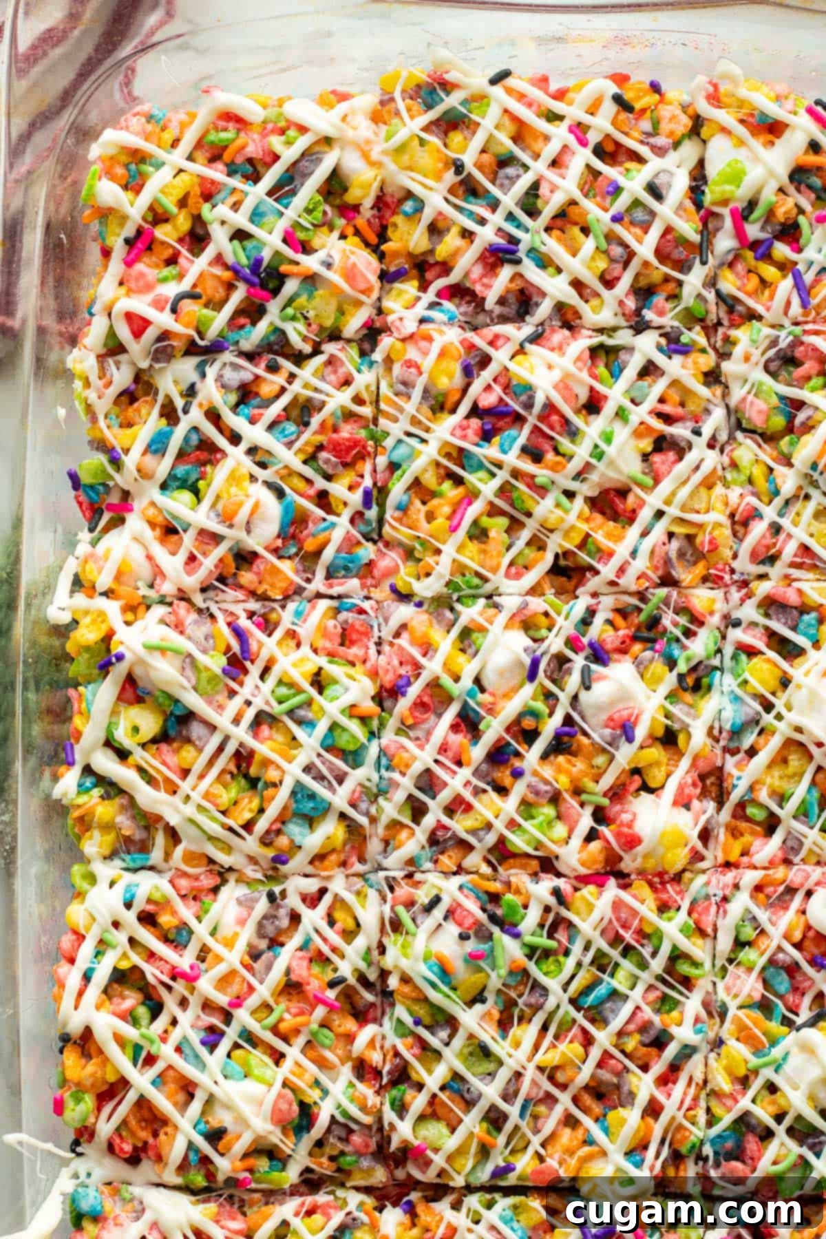 A pan of Fruity Pebble Rice Krispie Treats with a decorative white chocolate drizzle on top, ready for slicing.