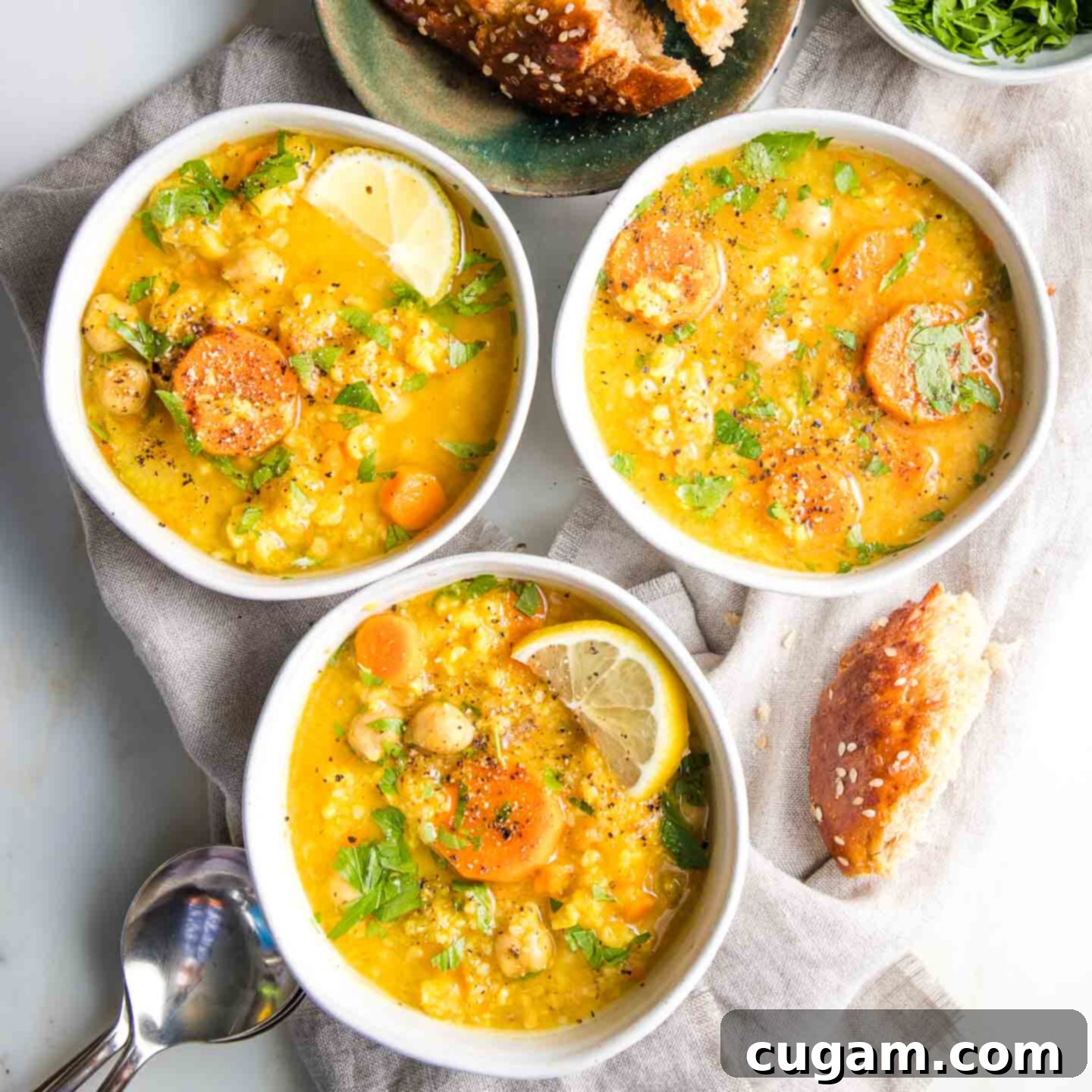 Nourishing Vegan Lemon Chickpea Rice Soup 14 Three bowls, filled with chickpea, rice, lemon and carrot soup, some crusts of bread lying around on a linen napkin with spoons on the side, inviting to be eaten.