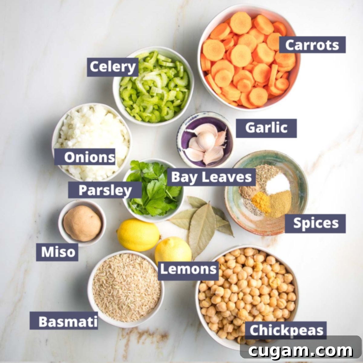 Nourishing Vegan Lemon Chickpea Rice Soup 4 Labeled ingredients for lemon chickpea rice soup: carrots, celery, onions, garlic, spices (cumin, coriander, turmeric, oregano), chickpeas, basmati rice, miso paste, fresh lemons, parsley, and bay leaves.