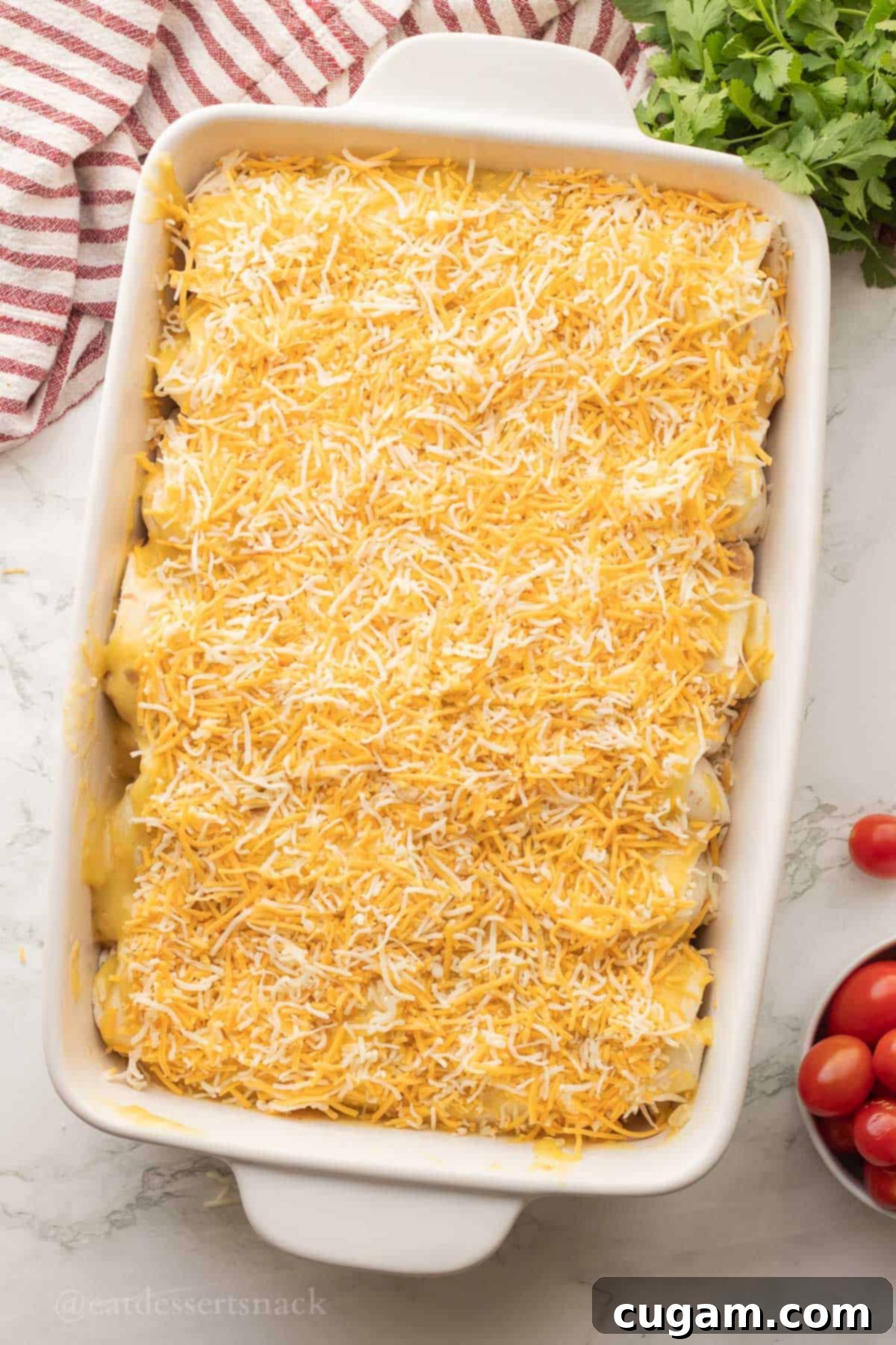 Shredded cheese generously sprinkled on top of enchiladas in a baking pan, ready for the oven.