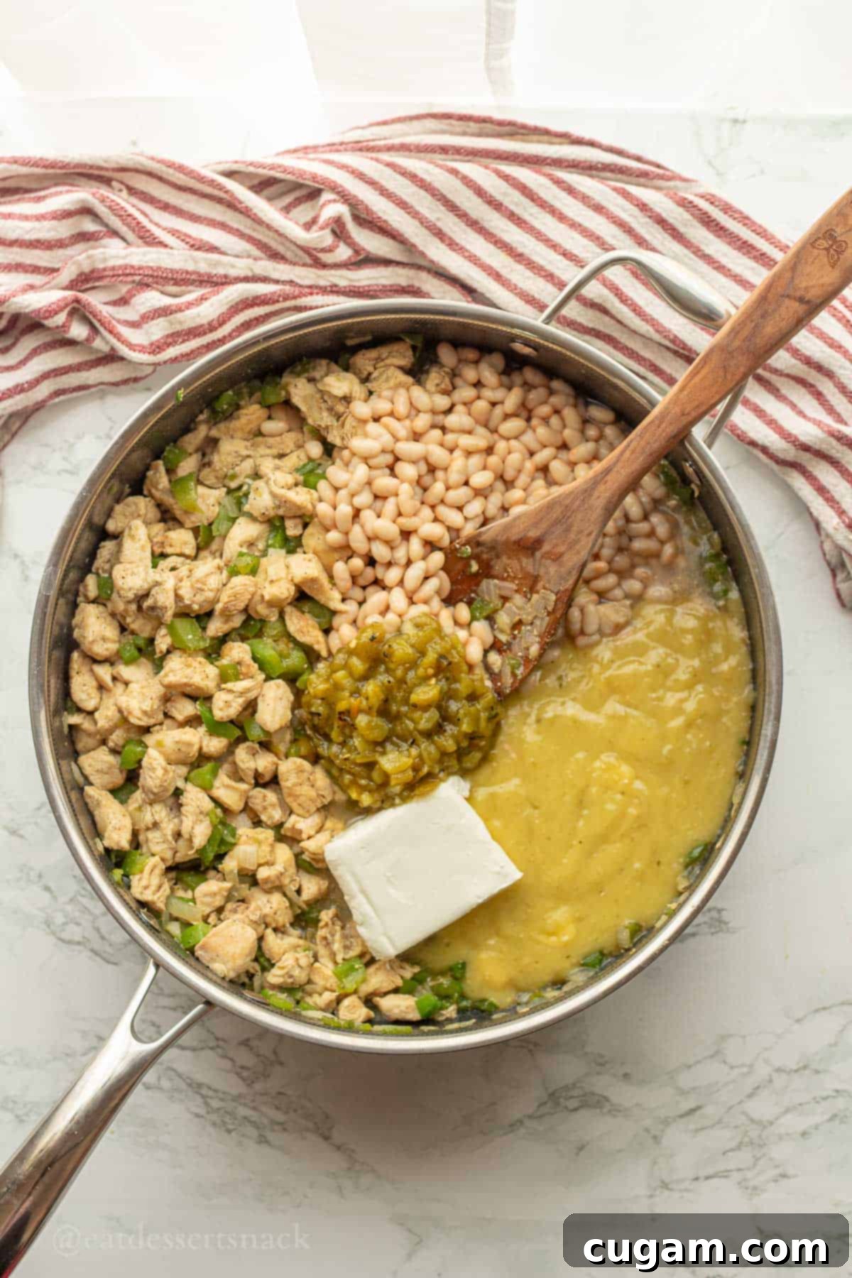 Combining beans, cream cheese, green chiles, and half of the salsa verde mixture into the chicken and vegetable filling in a metal pan with a wooden spoon.