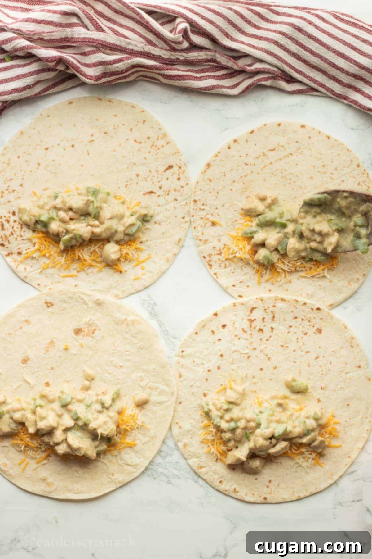 Tortillas being filled with shredded cheese and enchilada mixture, ready for rolling.