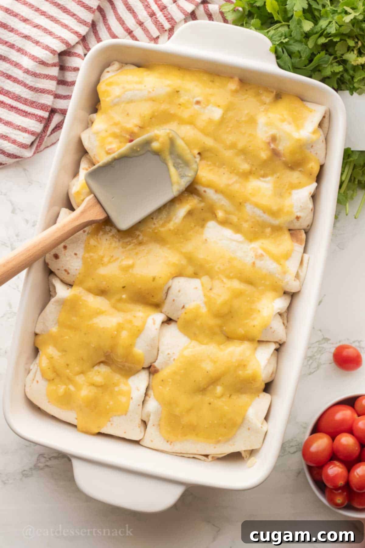 Spreading the remaining salsa verde mixture over assembled enchiladas in a baking pan, prior to adding more cheese.