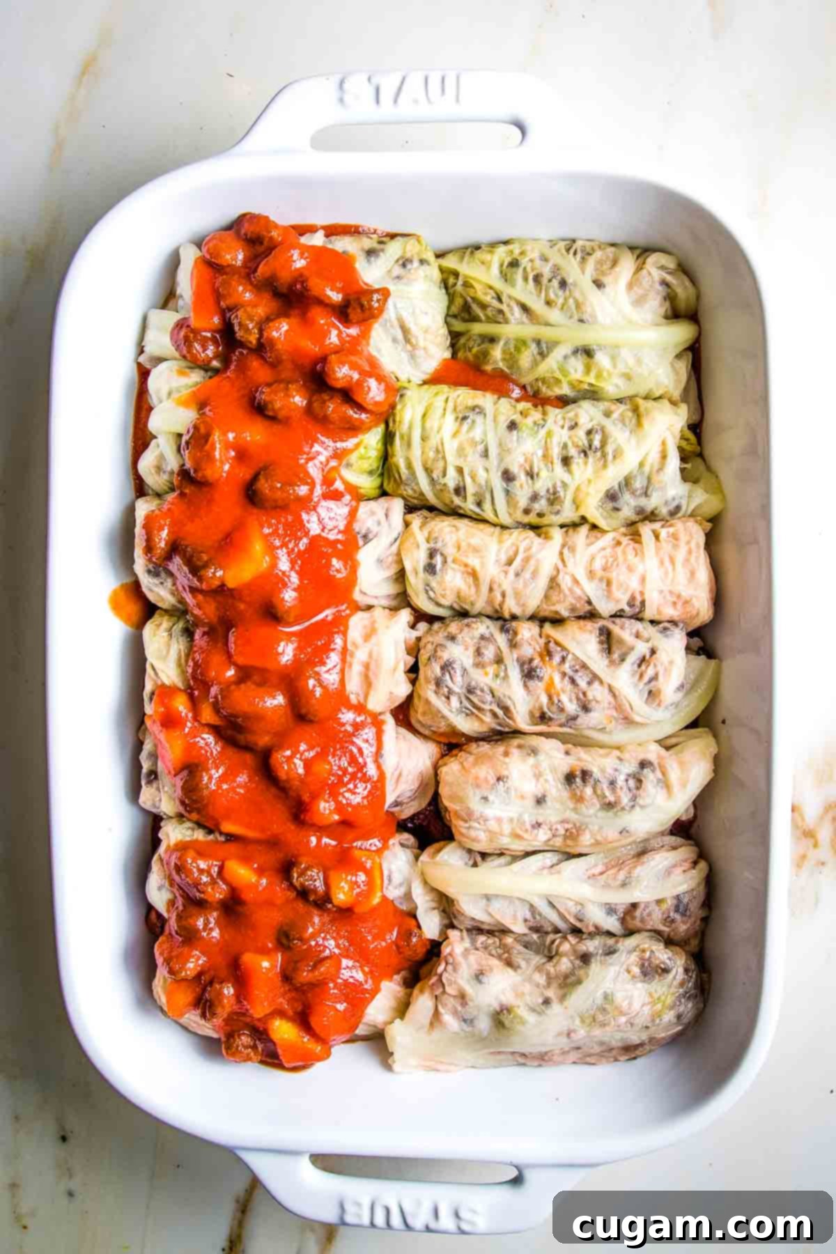 Hearty Vegan Cabbage Bundles 17 Stuffed cabbage rolls on top of sweet and sour sauce in a baking dish, adding more sauce on top.