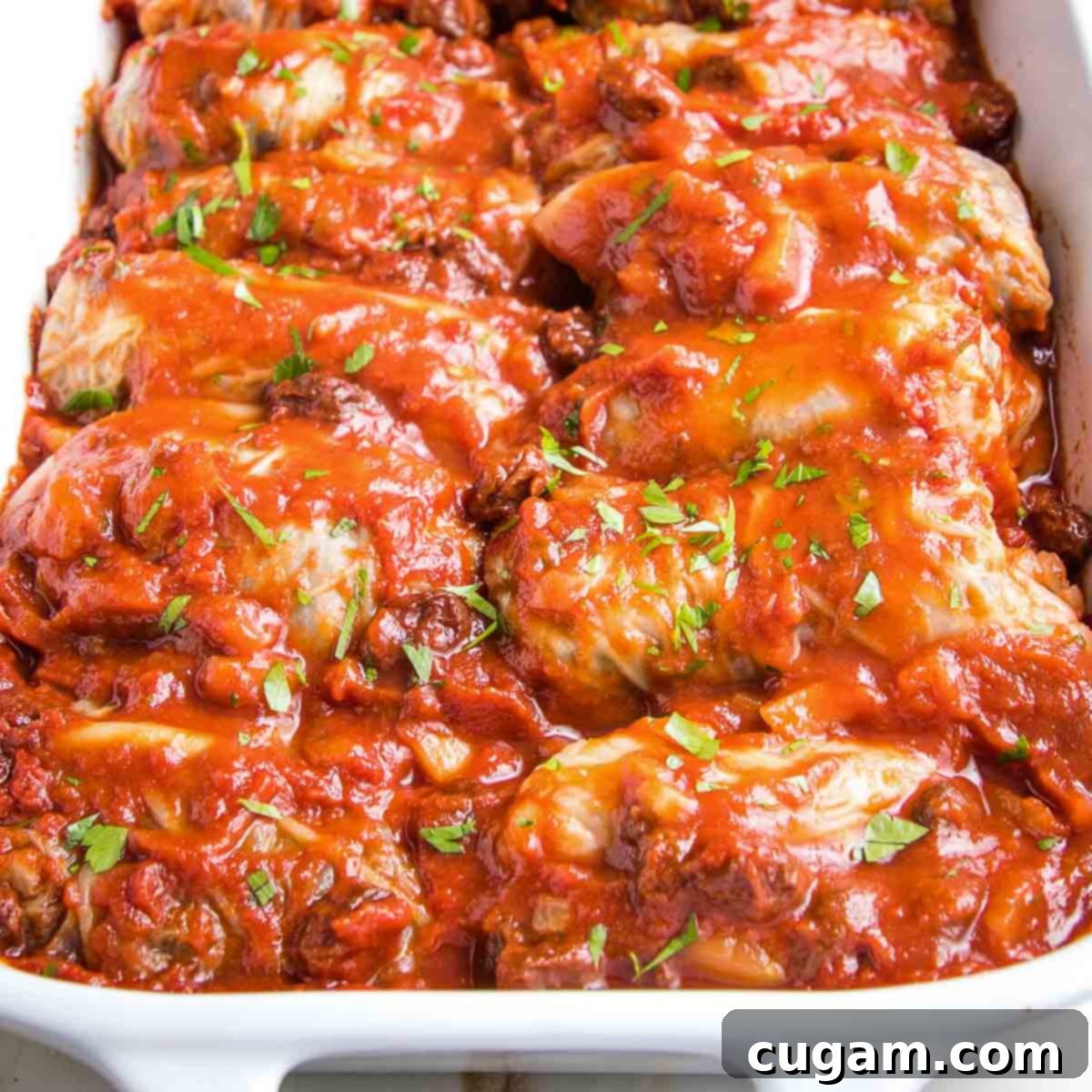 Hearty Vegan Cabbage Bundles 3 White baking dish with stuffed cabbage in red sauce with fresh herbs on top.