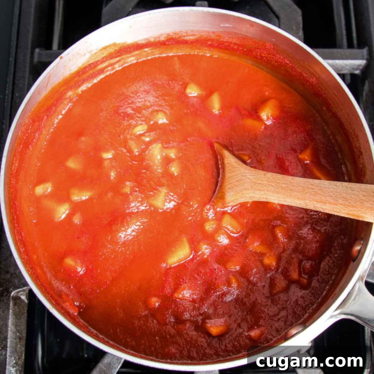 Hearty Vegan Cabbage Bundles 7 Saucepan with red sauce showing chunks of apples and raisins.
