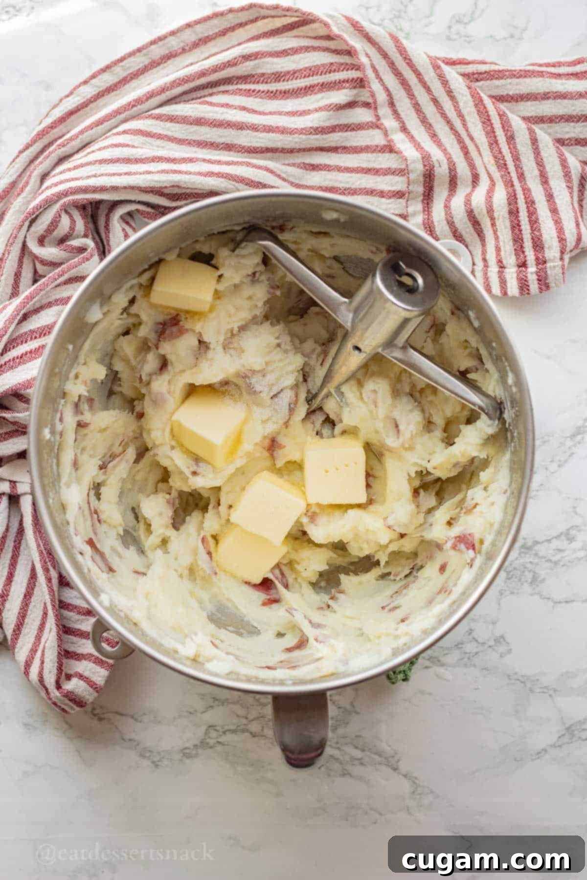Butter in mixing bowl with potatoes and paddle attachment.