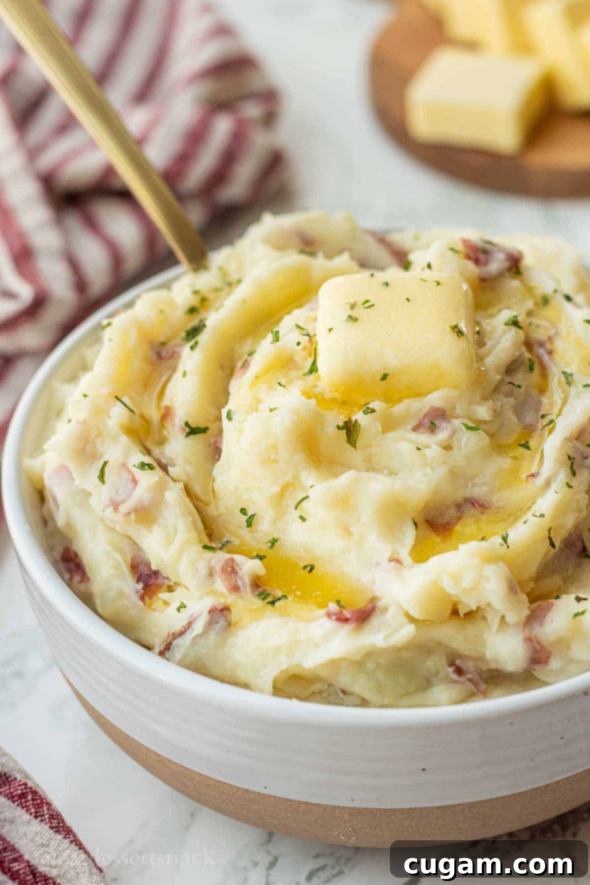 Red skin mashed potatoes with butter on top in white bowl with gold spoon.