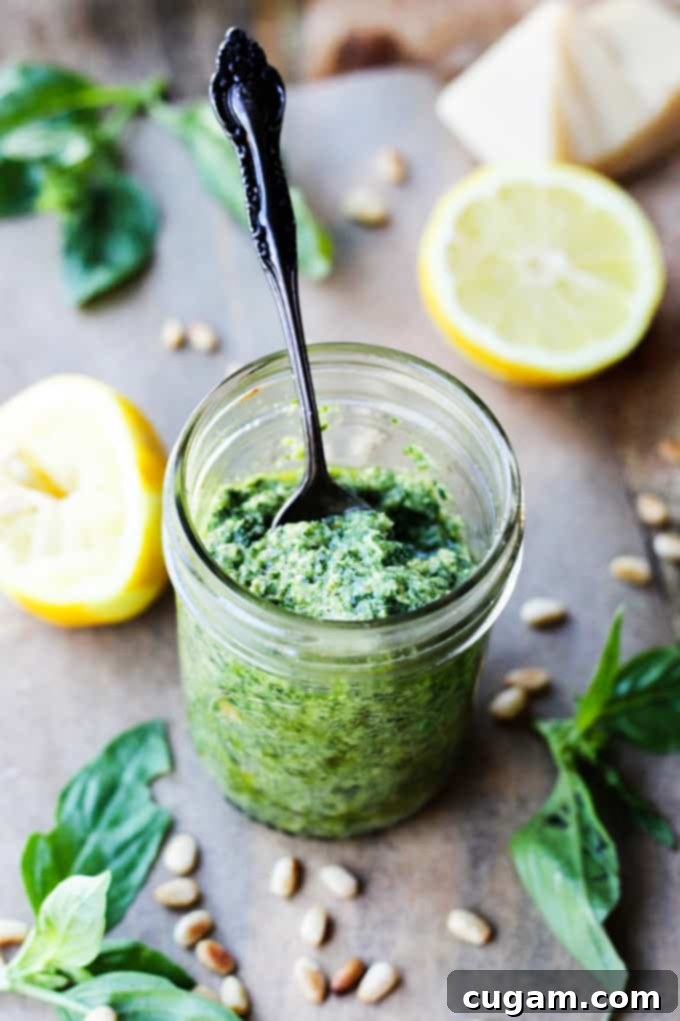 A glass jar filled with vibrant green Lemon Basil Pesto, with a spoon resting in it, showcasing its fresh texture.