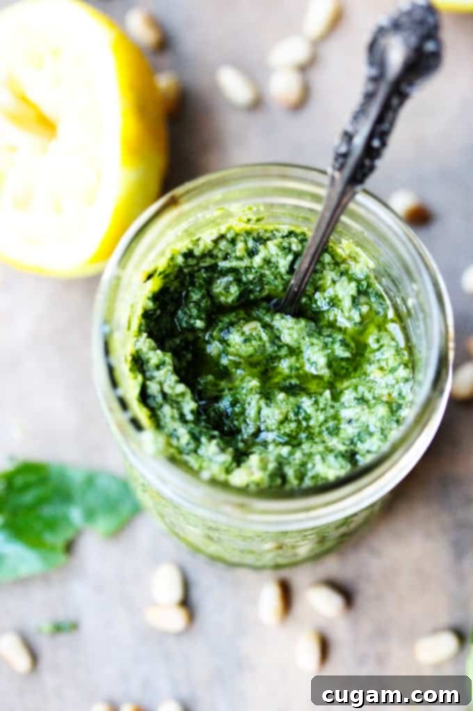 A spoonful of vibrant basil pesto sauce, with a fresh lemon cut in half in the background, emphasizing the citrus notes.