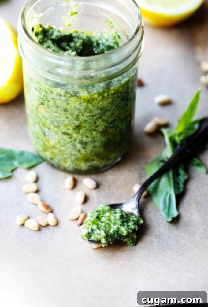 Close-up shot of basil pesto sauce on a spoon, with a jar of pesto visible in soft focus in the background, on a rustic surface.