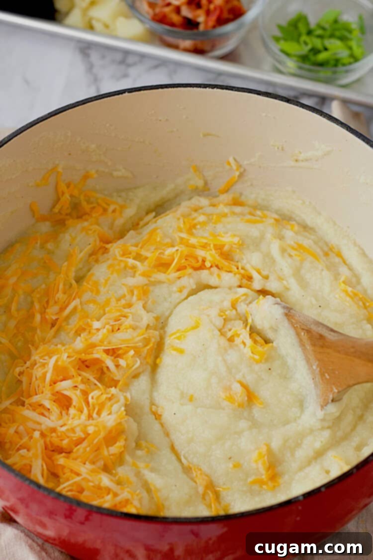Shredded cheddar cheese being stirred into a pot of creamy, cooked cauliflower and potato soup, melting into the rich liquid.