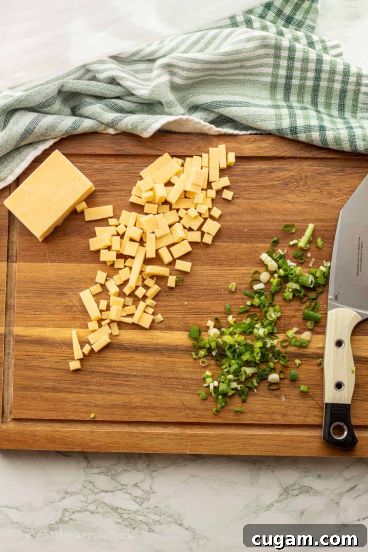 Chopped cheese and green onion on wood cutting board.