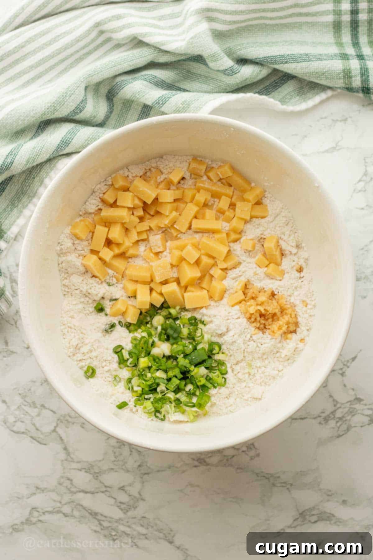 Cheese, garlic, and green onion in flour in white bowl.