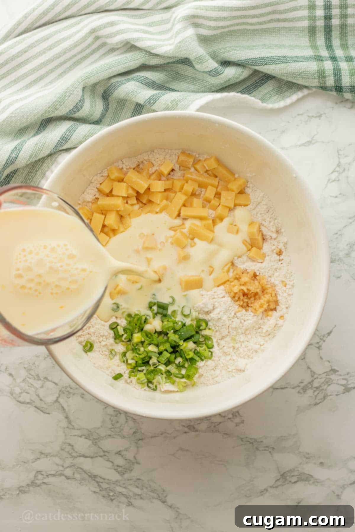 Pouring milk into dry ingredients in white bowl.