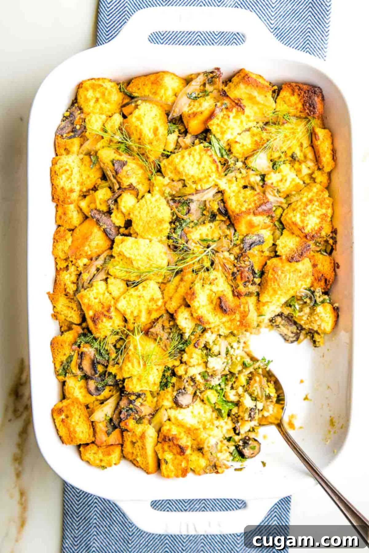 Cornbread stuffing with fresh herbs and mushrooms in a baking dish, garnished with fennel fronds and parsley.