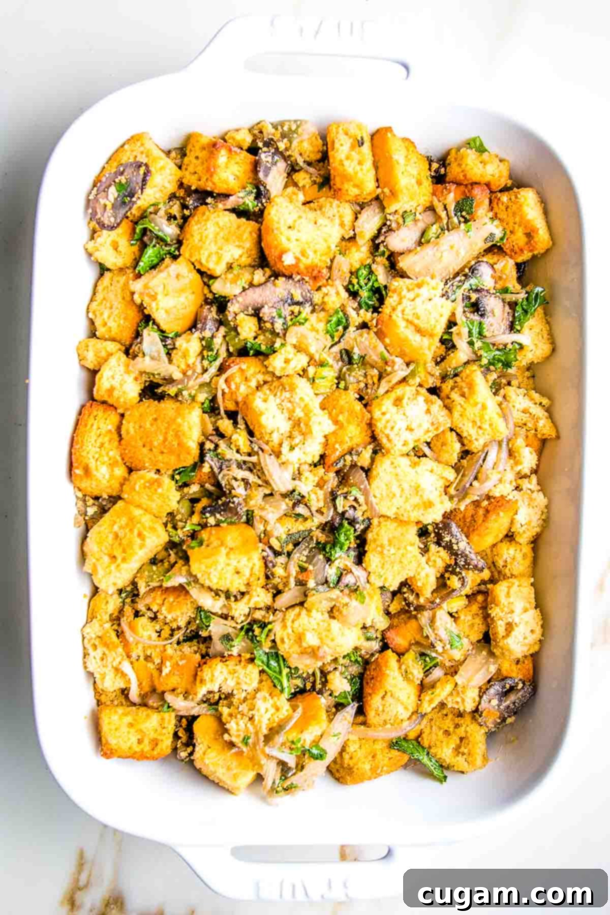 Cornbread cubes mixed thoroughly with sautéed mushrooms, herbs, and onions in a large bowl, showing the texture.