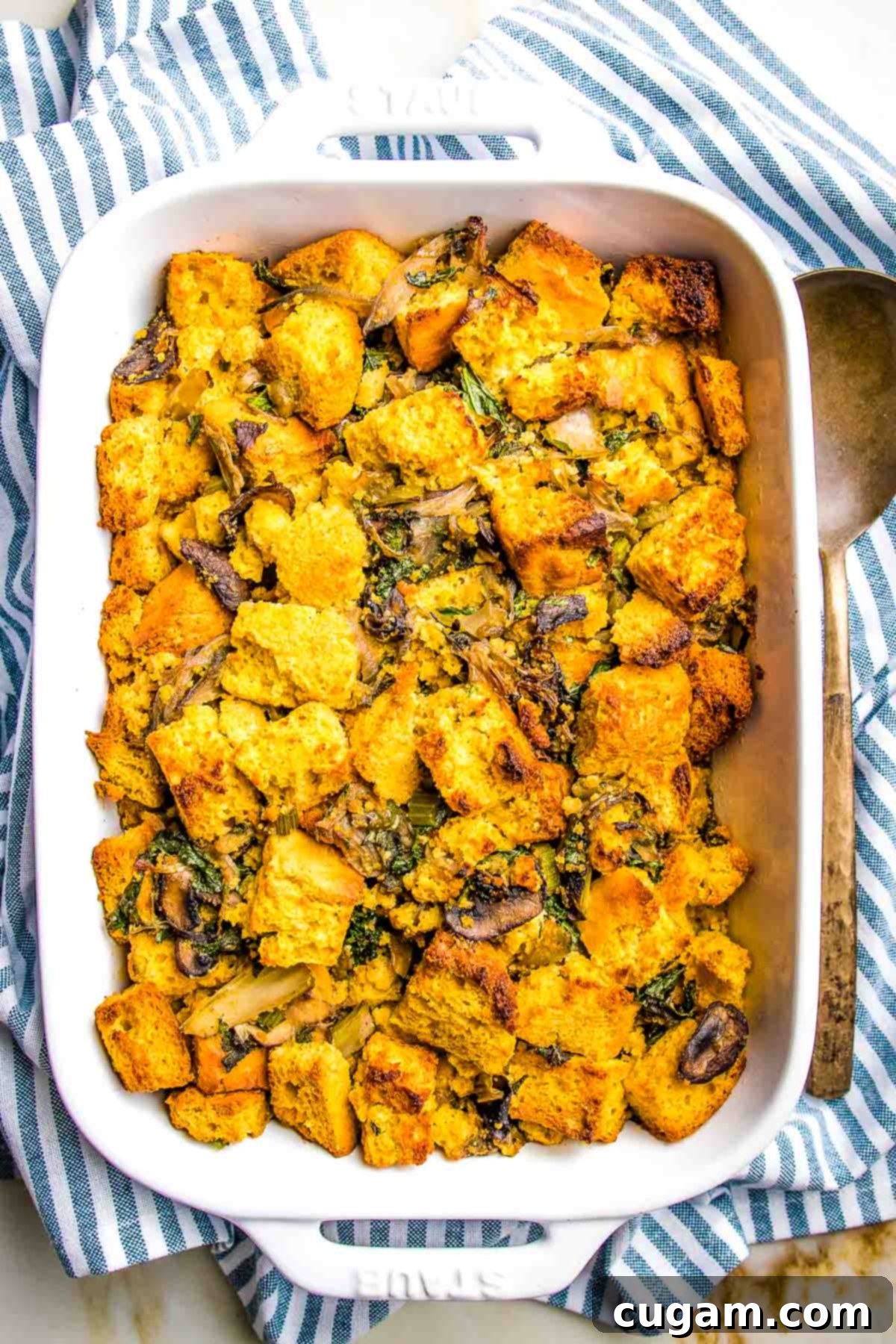 Unbaked gluten-free cornbread dressing with kale and mushrooms inside a white baking dish, vegetable stock just added, ready for the oven.