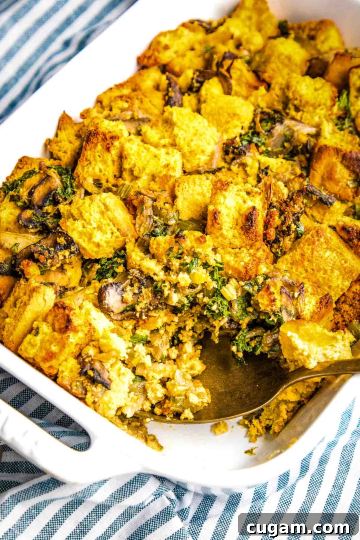Close-up of baked cornbread stuffing featuring mushrooms, herbs, and a crispy top in a baking dish, garnished with fresh herbs and ready to serve.