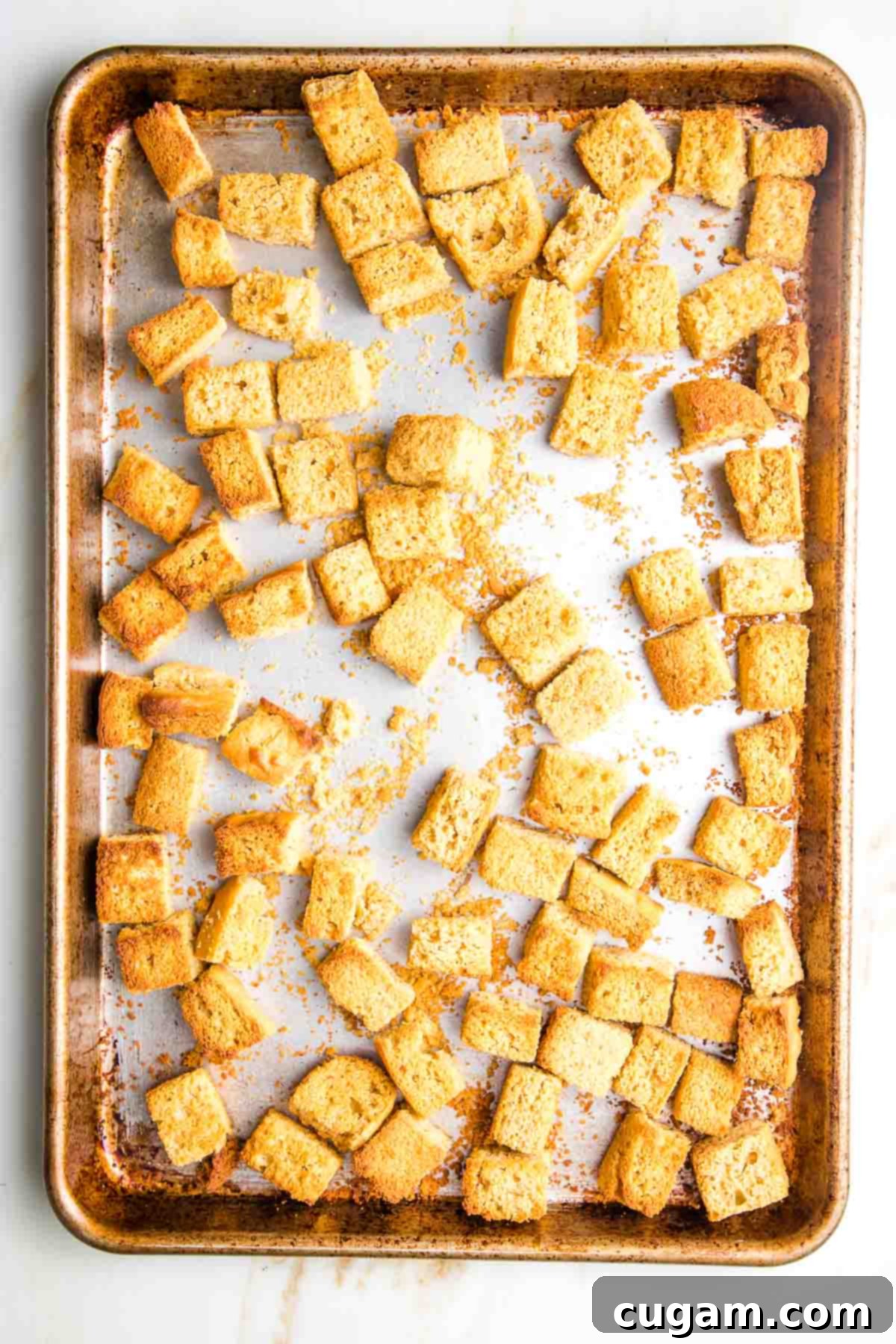 Toasted cornbread cubes on a large rimmed baking sheet, golden and crisp, ready for stuffing.