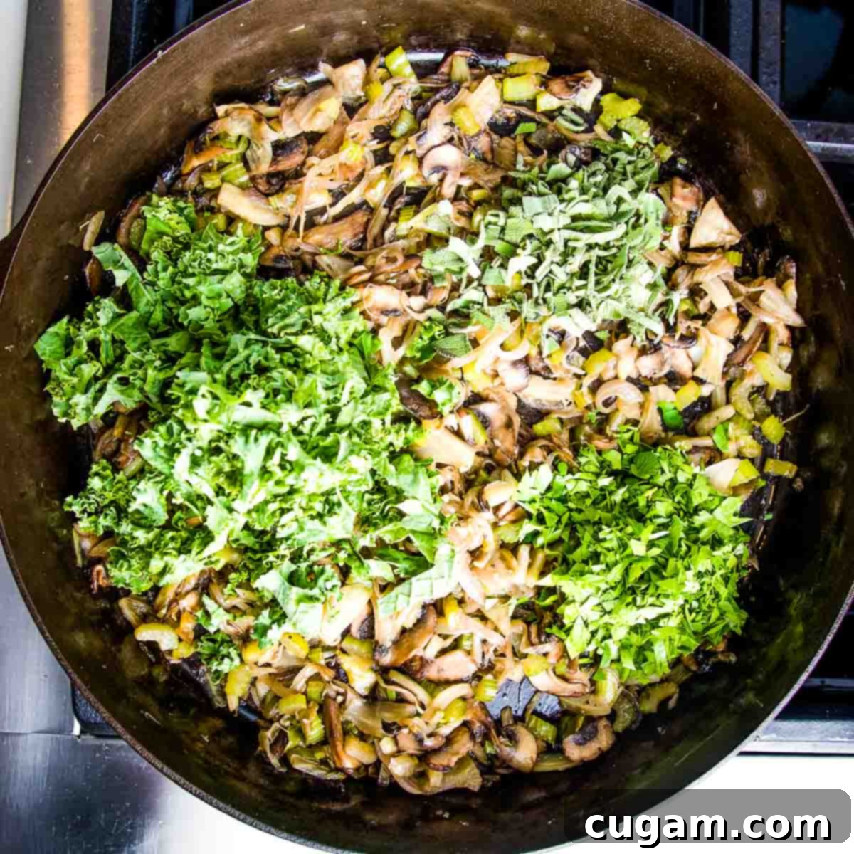 Fresh kale, chopped parsley, and sage added on top of warm sautéed vegetables in a cast iron skillet, ready to be mixed.