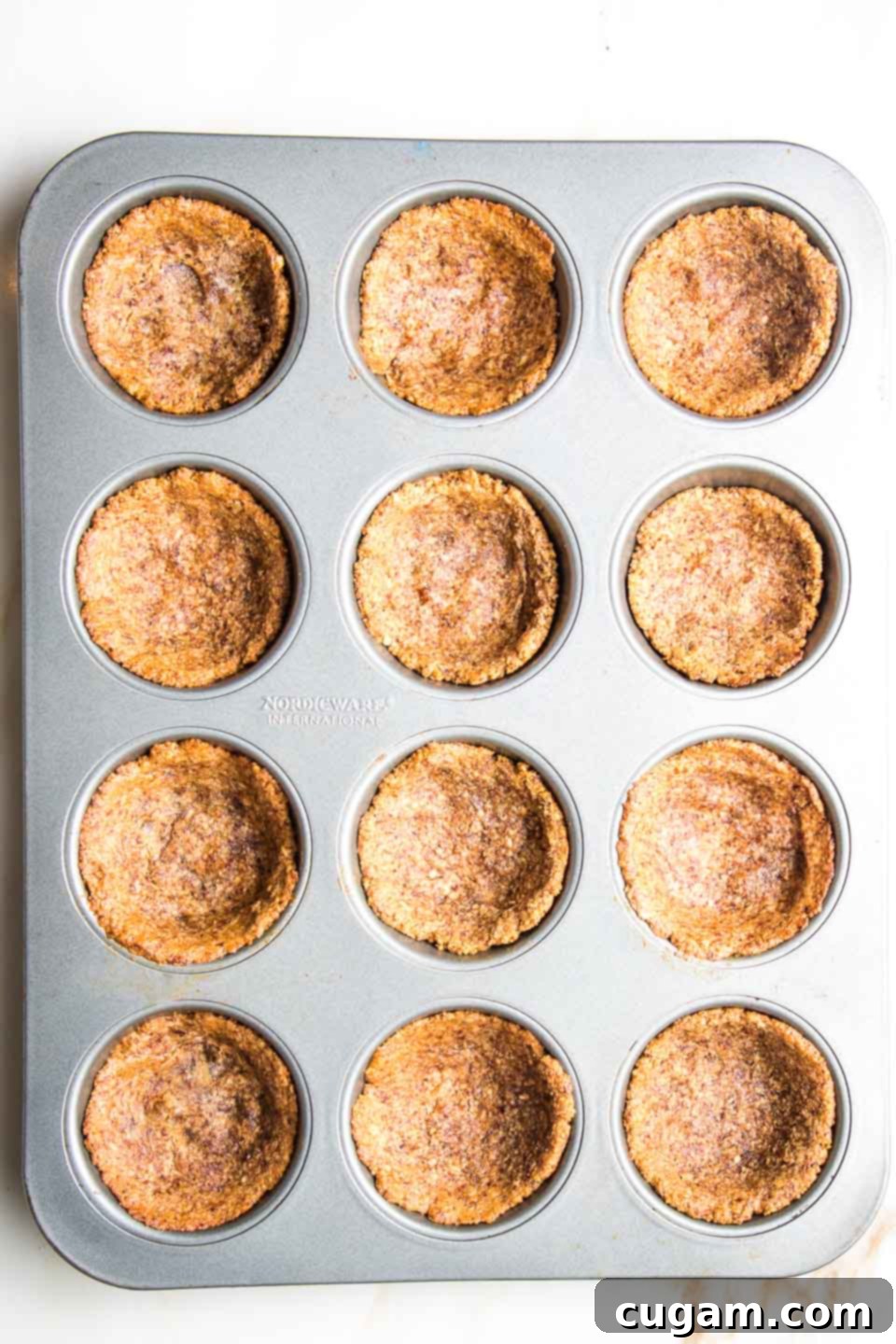 Pre-baked gluten-free mini pumpkin pie crusts in a muffin tin.