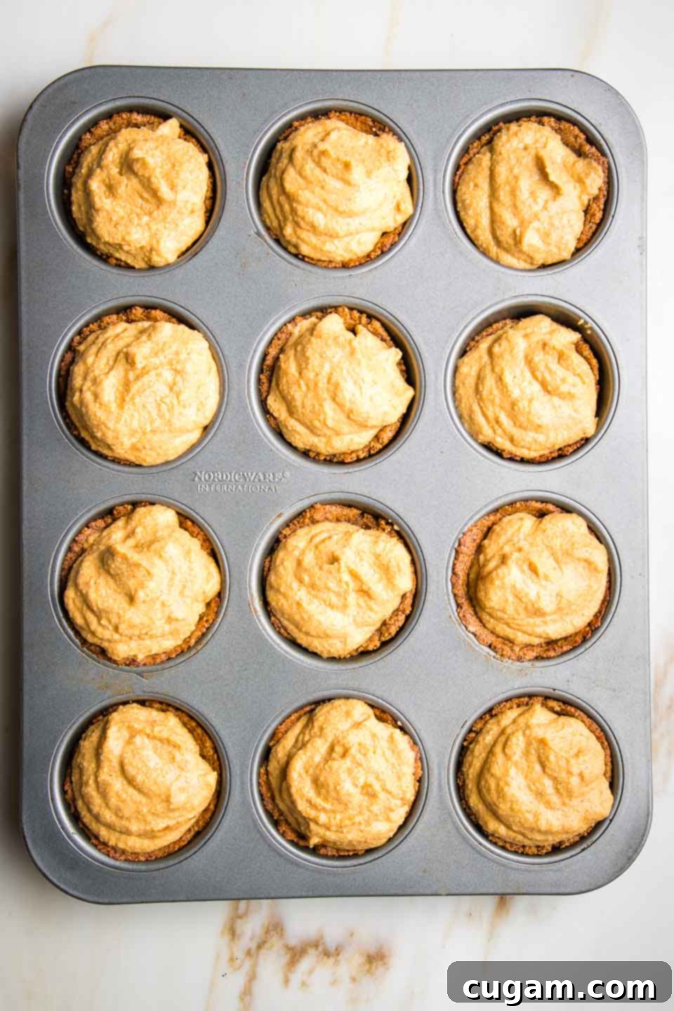 Mini pumpkin pies in a muffin tin, ready to bake.