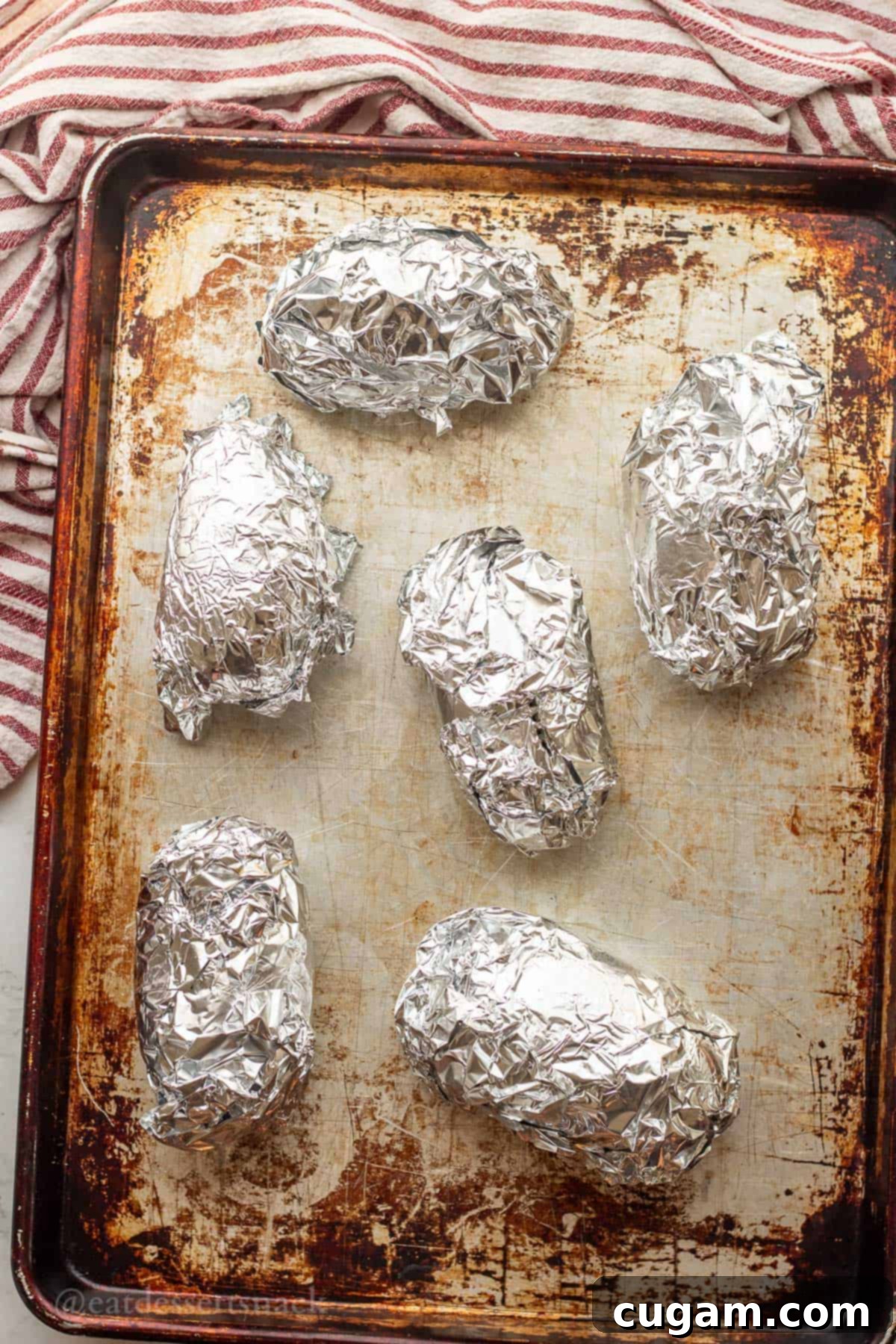 Chicken Bacon Ranch Baked Potatoes 4 Baked potatoes wrapped in tin foil on a baking sheet, ready for the oven.