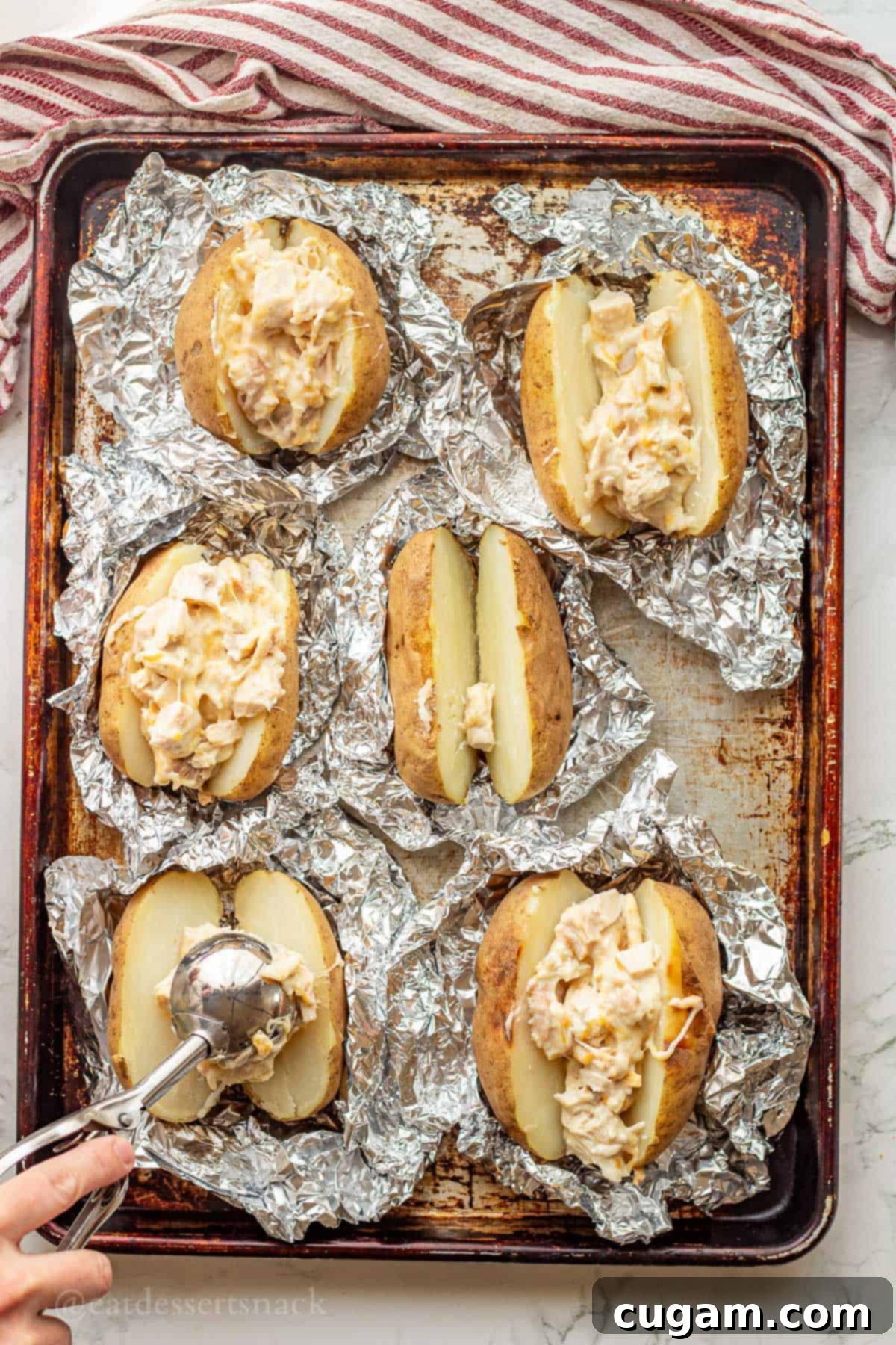 Chicken Bacon Ranch Baked Potatoes 8 Scooping cheesy chicken ranch filling into sliced baked potatoes on a baking sheet, preparing for the final bake.