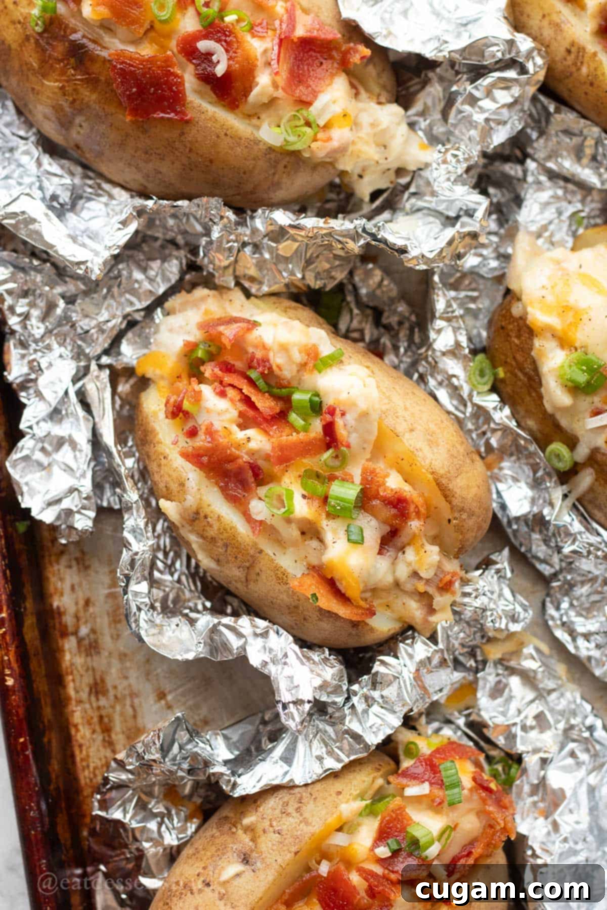 Chicken Bacon Ranch Baked Potatoes 10 Baked potatoes generously topped with cheese, crispy bacon, creamy ranch filling, and fresh green onions, resting on tin foil.