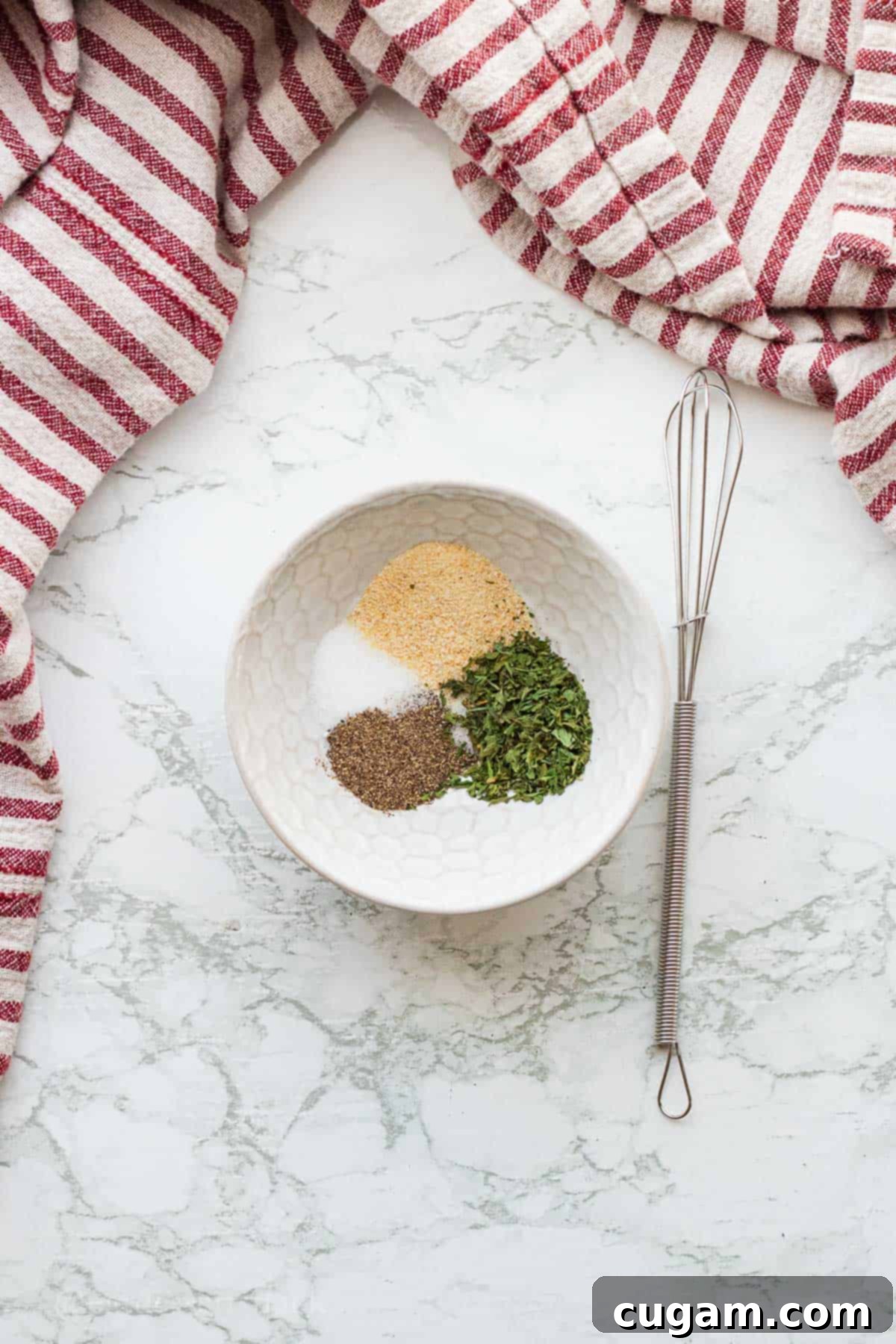 Spice mixture in white bowl with wire whisk.