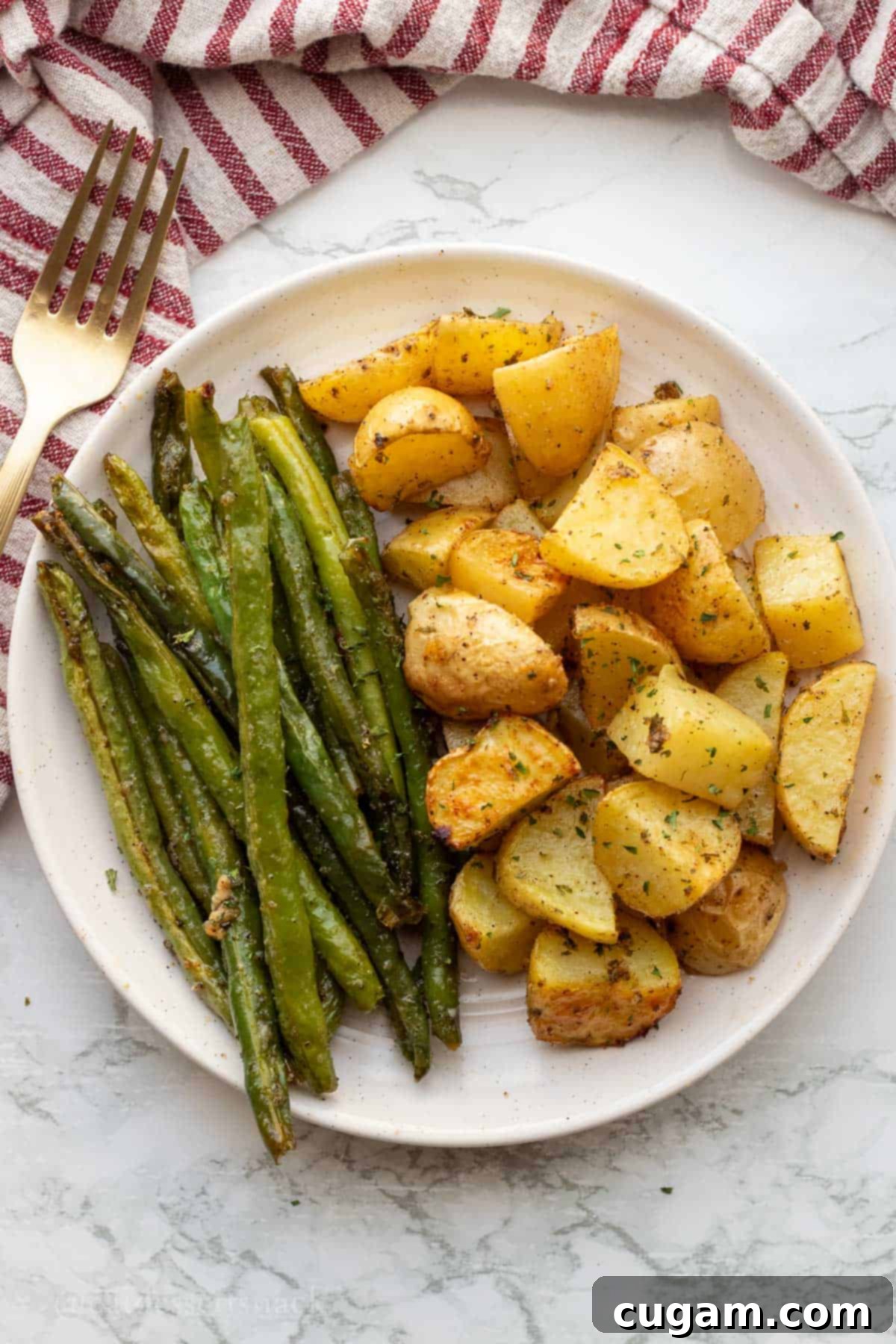 Baked green beans and potatoes on white plate on marble countertop with gold fork.
