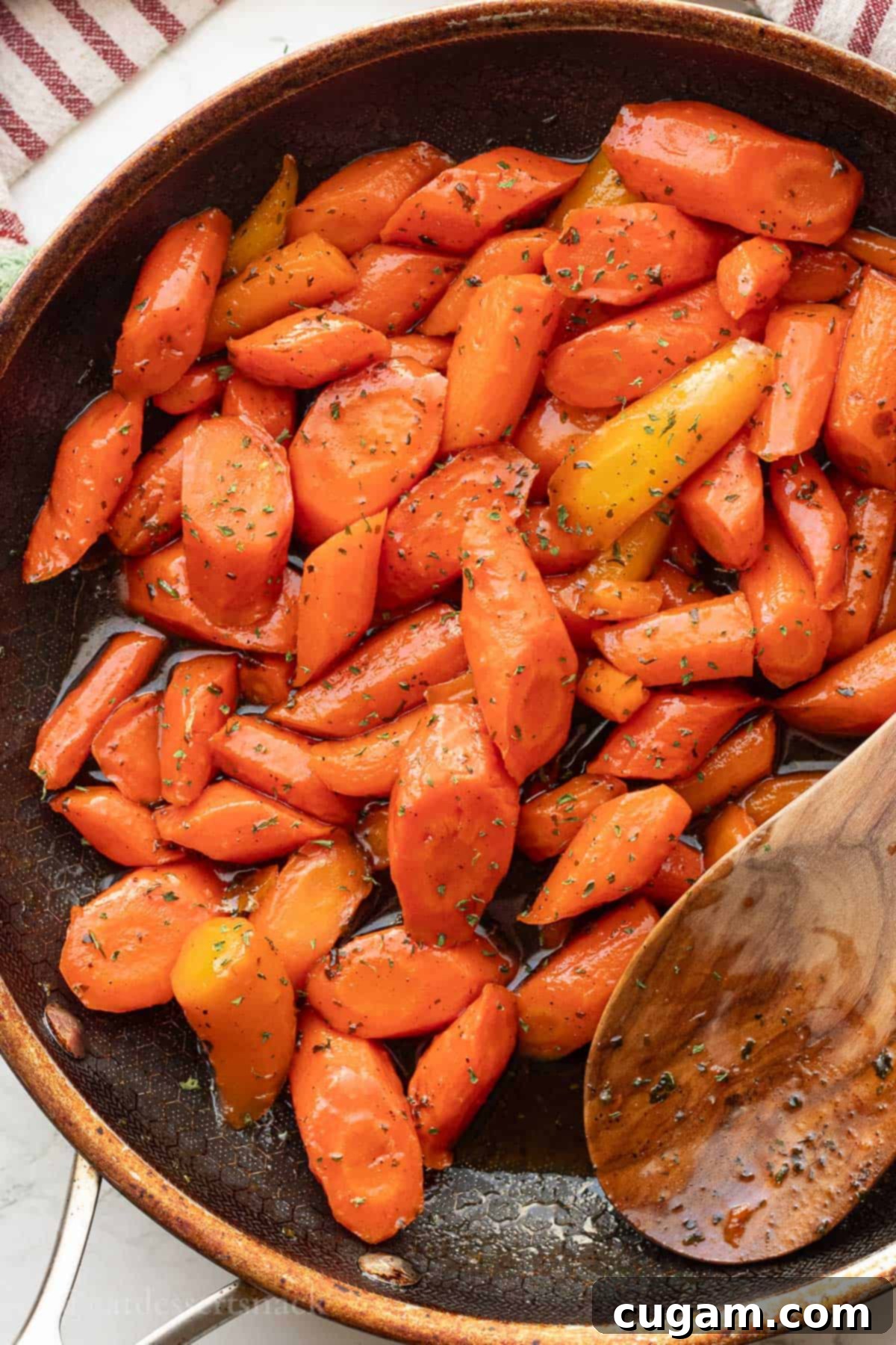 Cooked glazed carrots in black frying pan with wooden spoon, perfectly caramelized and ready to serve.