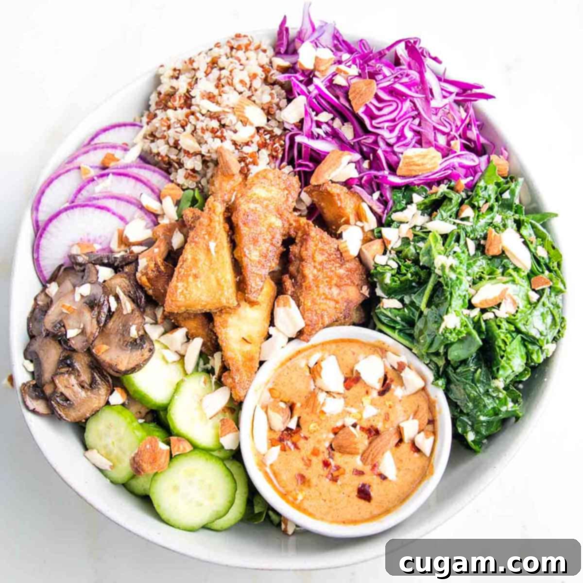 Crispy tofu in a bowl with red cabbage, sauteed greens, mushrooms, raw veggies and an almond butter sauce.
