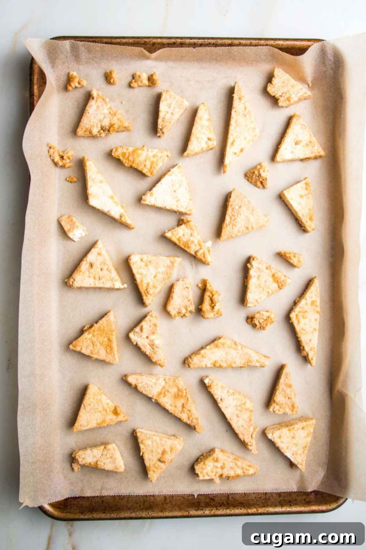 Small triangles of tofu, spread on a parchment lined baking sheet.