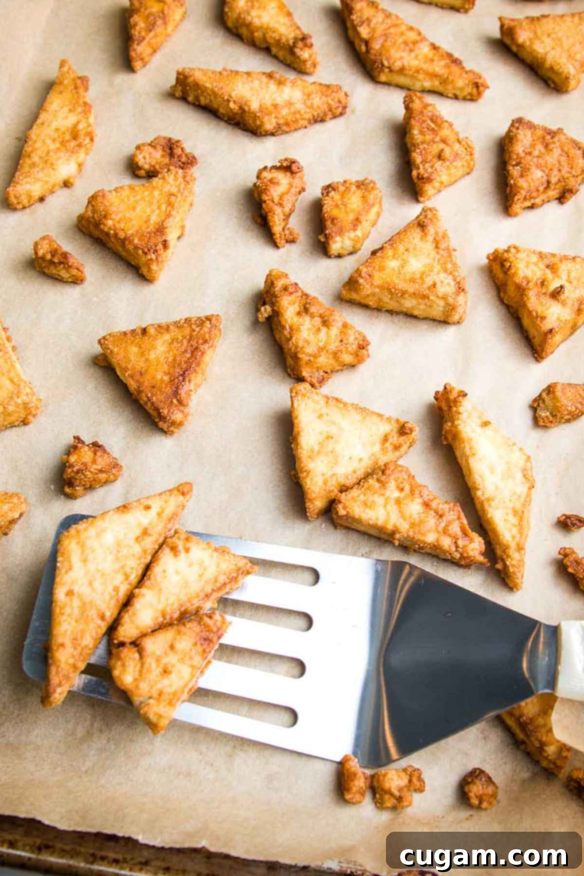 Crispy pieces of tofu coming off a parchment lined baking sheet. 
