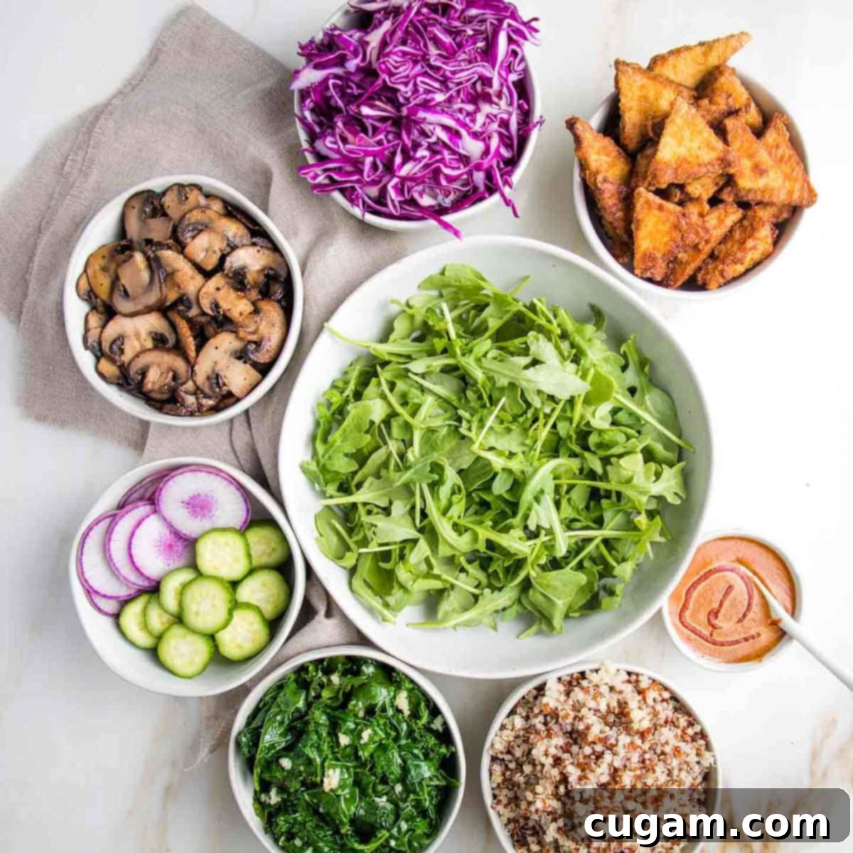 Bowl of greens in center surrounded by bowls of cooked and raw veggies plus crispy tofu.