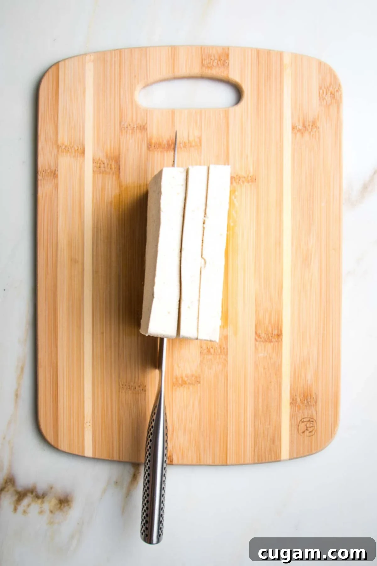 Block of tofu turned on its side, showing it being cut into 3 equal portions. 